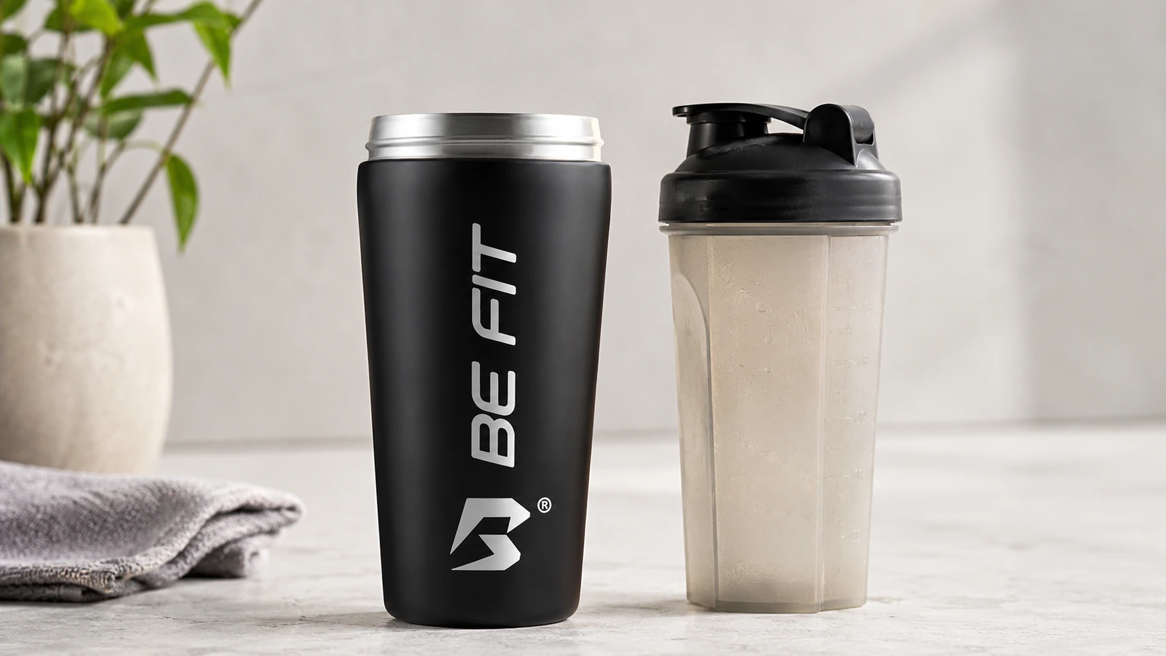Zwarte RVS BE FIT shakebeker naast gebruikte plastic shakebeker als alternatief