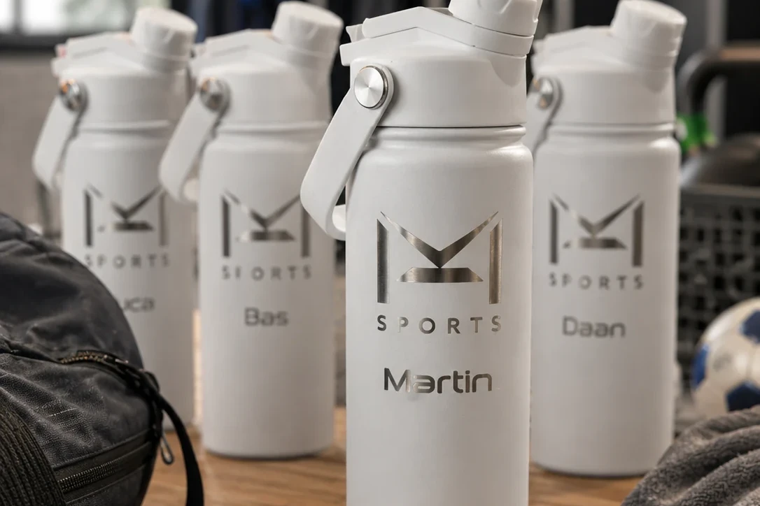 Meerdere gegraveerde sportflessen met M Sports logo en namen Martin, Bas en Daan klaar voor teamgebruik in een sportomgeving.