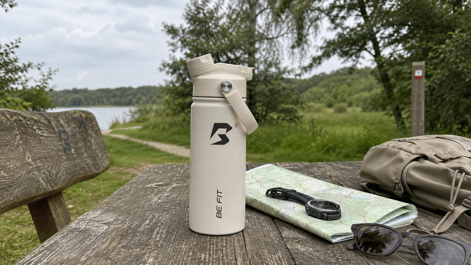 BE FIT SWIGGER naast een wandelkaart, horloge, zonnebril en rugzak voor het plannen van water tijdens een wandeling